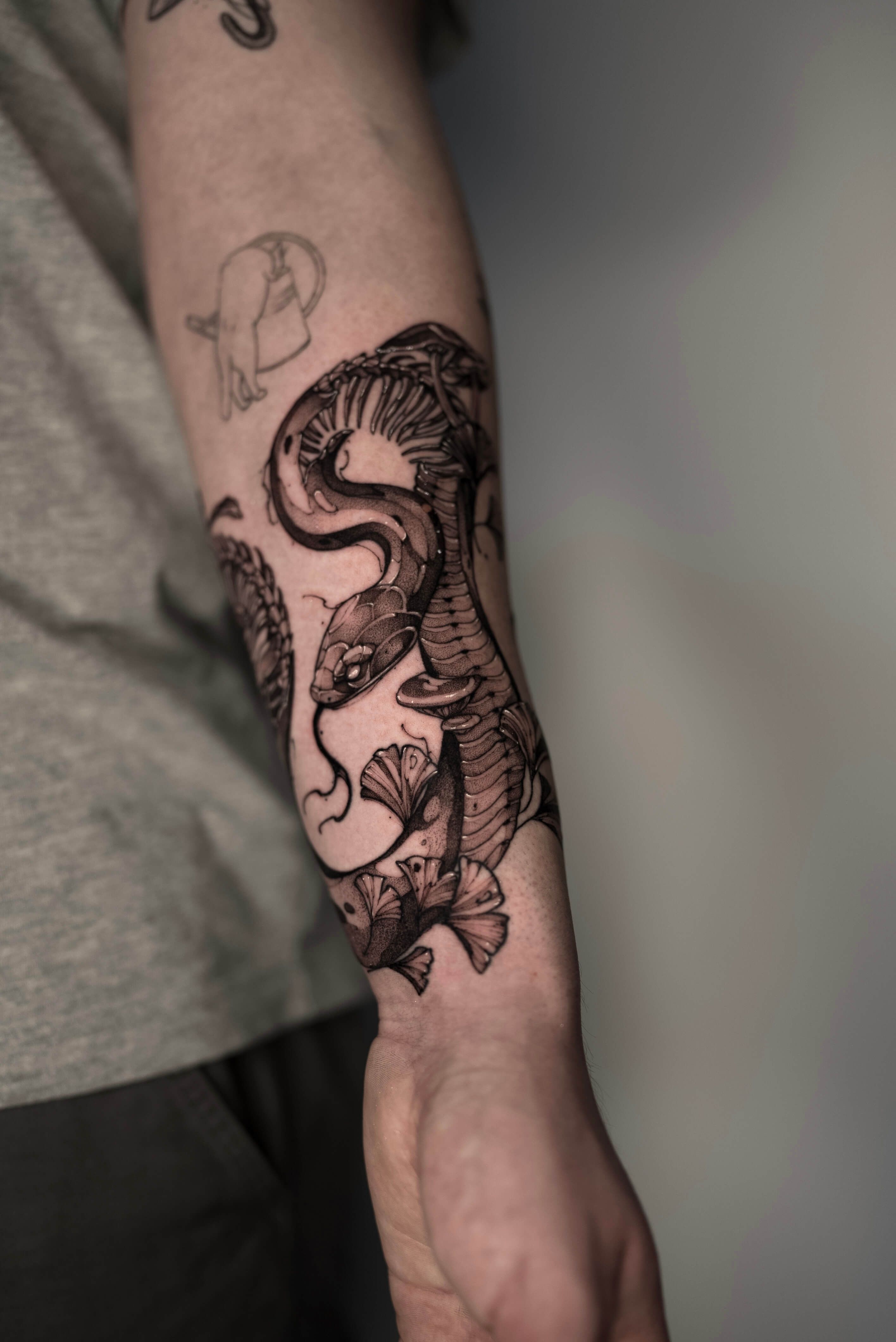 Large cobra snake and ginkgo botanical tattoo wrapping the forearm — tattoo Barcelona