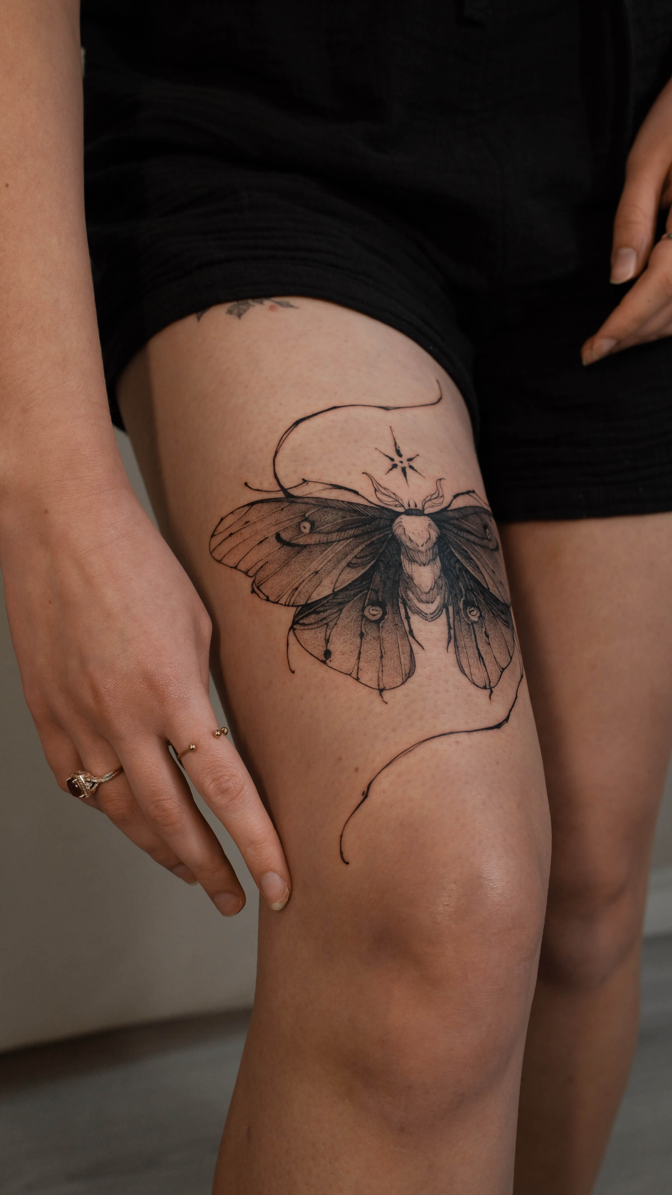 Fine line moth tattoo with star on thigh — tattoo Barcelona