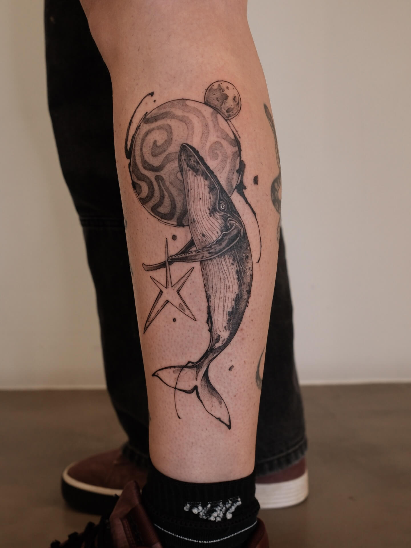 Graphic tattoo of a whale with cosmic moon and star on calf — tattoo Barcelona